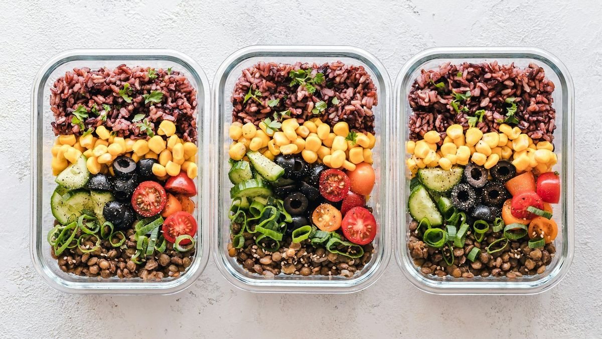 Three glass meal prep containers filled with grains, beans, olives, tomatoes and vegetables