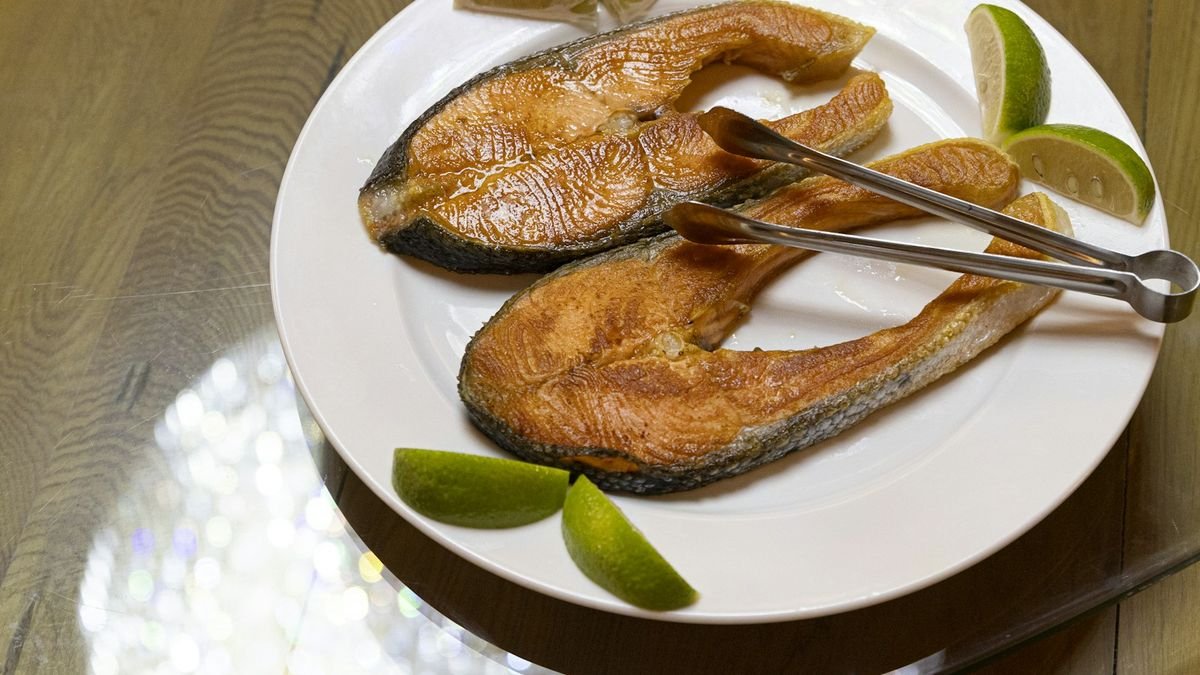 Two cooked salmon steaks with lime wedges on a white plate; fatty fish like salmon are among the richest sources of the omega-3s EPA and DHA